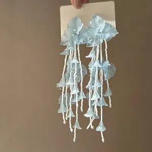 Close-up detail view of elegant light blue acrylic flower tassel earrings with beads