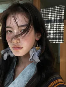 Close-up view of grey feather tassel drop earrings with a luxurious gold finish on model