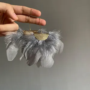 Hand-held detail of elegant grey feather fringe earrings with gold hammered crescents.