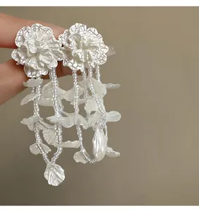Close-up of white floral drop earrings with beaded tassels and petal accents