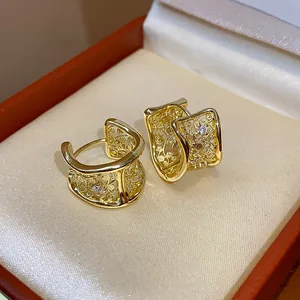 Dettaglio di orecchini dorati geometrici con traforo floreale e strass incastonato.