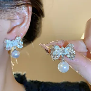 Detail shot of elegant silver bow earrings with dangling white pearls and textured finish.