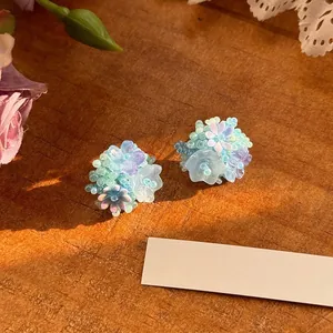 Macro view of colorful beaded flower earrings with iridescent finish on wood background.