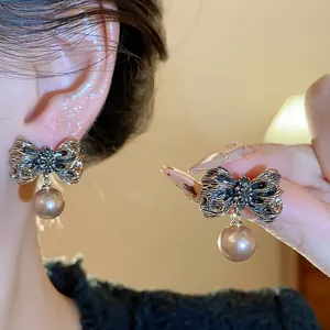 Macro view of elegant vintage gold wrinkled bow-knot earrings with a hanging pearl drop