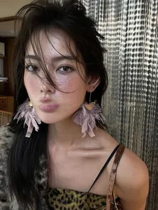 Detail view of pink feather tassel earrings worn by a model
