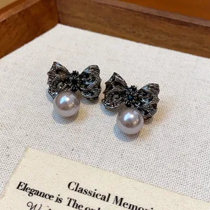 Detailed view of pleated dark metallic bow earrings featuring elegant grey pearl drops