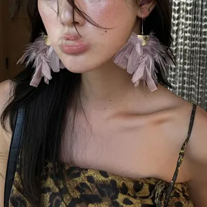 Detailed close-up view of a model wearing elegant purple feather tassel earrings with gold hooks