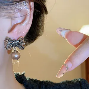 Close-up view of elegant vintage-style bow earrings with a hanging pearl on model's ear