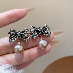 Macro view of vintage textured bow stud earrings with elegant dangling pearls