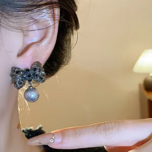 Detailed close-up of elegant pleated bow stud earrings with a grey pearl on model ear