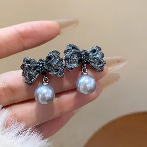 Detailed macro shot of wrinkled metallic bow earrings with elegant grey pearl drops.