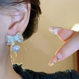 Detailed close-up shot of textured silver bow stud earrings with a dangling pearl