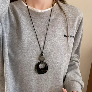 Gros plan d'un long collier de style Zen avec pendentif circulaire noir sur un sweat