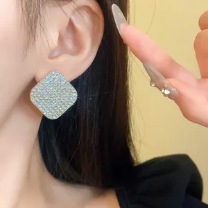 Gros plan d'une boucle d'oreille carrée en strass sur l'oreille du modèle