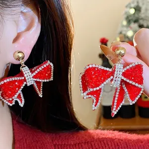 Elegant red resin bow earrings with rhinestone edges on a festive Christmas background.