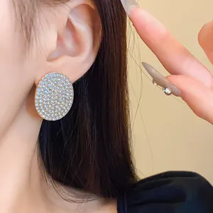 Vue détaillée d'une boucle d'oreille ovale sertie de strass brillants sur l'oreille d'un mannequin