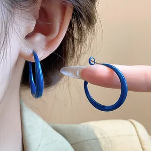 Elegant Klein Blue hoop earrings with silver needle shown worn on ear and held in hand.