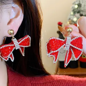 Detail view of sparkling red resin bow earrings with rhinestone edges and silver needle.