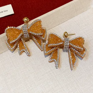 Detailed close-up view of elegant amber resin bowknot earrings with sparkling rhinestones.