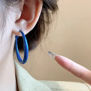 Close-up view of vibrant Klein blue hoop earrings on ear featuring retro matte finish