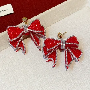 Close-up of red resin bow earrings with sparkly rhinestone borders and gold studs