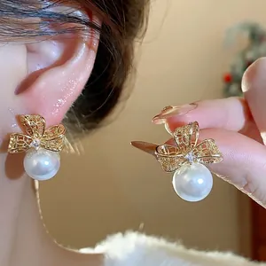 Eleganti orecchini a fiocco in perla placcati oro con zirconi indossati e tenuti