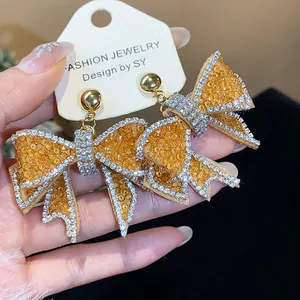 Close-up of elegant sparkling bow-shaped earrings with yellow resin and rhinestones