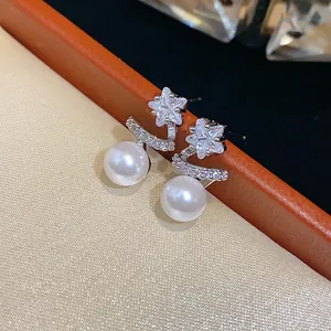 Macro detail of star-shaped zircon and pearl stud earrings on cream fabric background