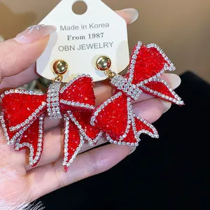 Close-up of sparkly red rhinestone bow earrings with gold studs on a display card.