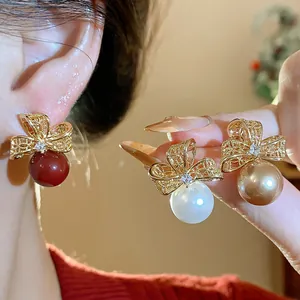 Dettaglio di orecchini a fiore traforati placcati oro con perle rosse, bianche e champagne.
