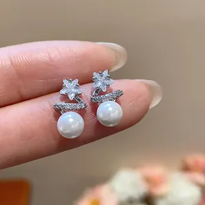 Detail showing silver star zircon stud earrings with elegant white pearls on fingers.