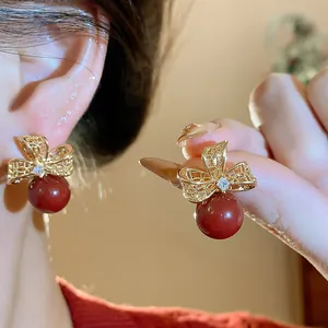 Vista dettagliata di orecchini a fiocco cavo placcati oro con zircone e perla rossa.