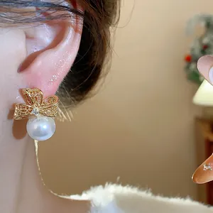 Primo piano di orecchino a fiocco con perla e zirconi placcato oro indossato su orecchio.