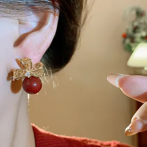 Dettaglio di eleganti orecchini a fiocco dorati con perle rosse e accenti di zircone