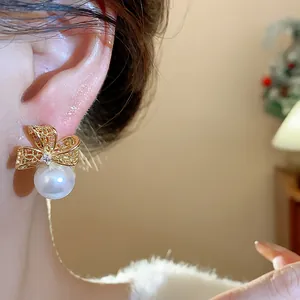 Primo piano di un elegante orecchino a fiocco dorato con perla bianca lucida.