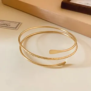 Detailed macro view of a gold spiral open bangle featuring textured and smooth metal finishes