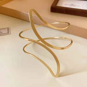 Detail of a gold-toned sculptural open cuff bracelet with fluid leaf-like design.