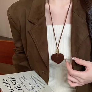 Primo piano di una collana con ciondolo a cuore marrone indossata con un blazer chic.