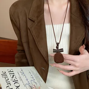 Dettaglio di una collana con pendente geometrico in resina marrone floccata autunnale.