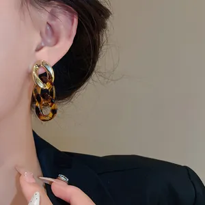 Close-up of geometric gold and amber resin chain earrings on a model wearing a black blazer.