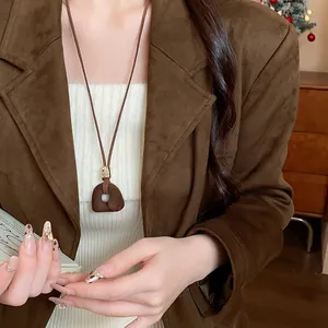 Dettaglio di una collana con ciondolo geometrico marrone su una giacca di camoscio.