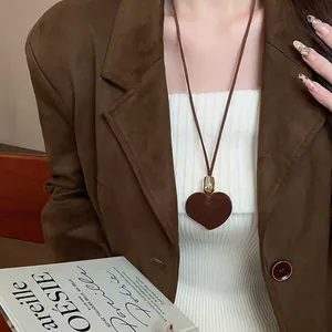 Dettaglio ravvicinato di una collana con cuore marrone floccato indossata con un blazer