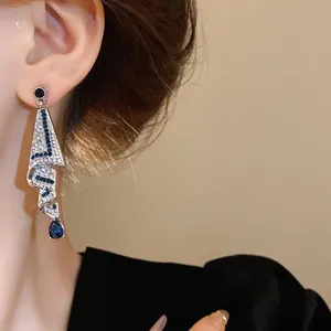 Close-up view of elegant silver needle drop earrings with blue and white crystals.