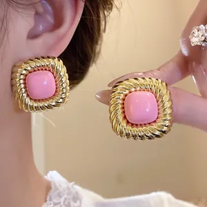 Dettaglio di orecchini vintage quadrati dorati con elegante pietra rosa centrale