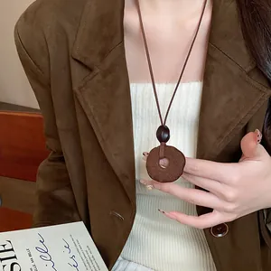 Primo piano di una collana con ciondolo in resina marrone su giacca di camoscio.