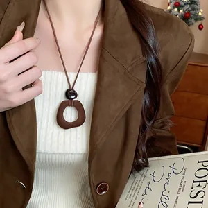 Dettaglio di una collana con ciondolo geometrico in resina marrone floccata su blazer.