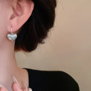 Dettaglio di orecchini a cuore in argento spazzolato con strass.