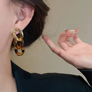 Close-up of elegant gold and tortoiseshell resin chain link dangle earrings on model