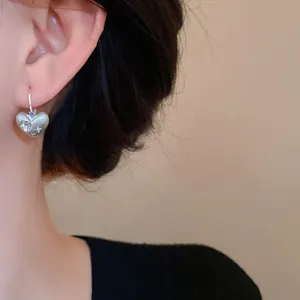 Dettaglio macro di orecchini a cuore in argento con trama spazzolata e piccoli strass