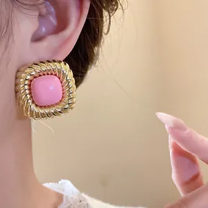 Primo piano orecchino vintage quadrato con pietra rosa e trama dorata intrecciata.